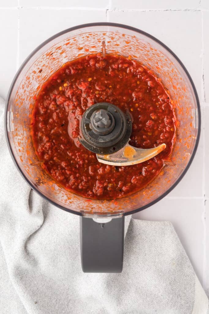 Blended chipotle honey sauce mixture inside a food processor bowl with visible red pepper and chili flecks.
