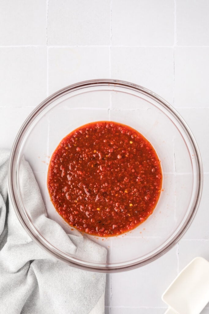 Chipotle honey sauce transferred into a glass bowl, smooth and vibrant red with specks of seasoning.