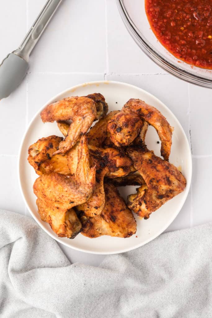 Crispy golden brown cooked chicken wings on a white plate with a bowl of chipotle honey sauce beside them.