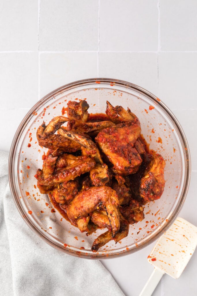 Cooked chicken wings tossed in chipotle honey sauce inside a glass bowl with a white spatula resting nearby.