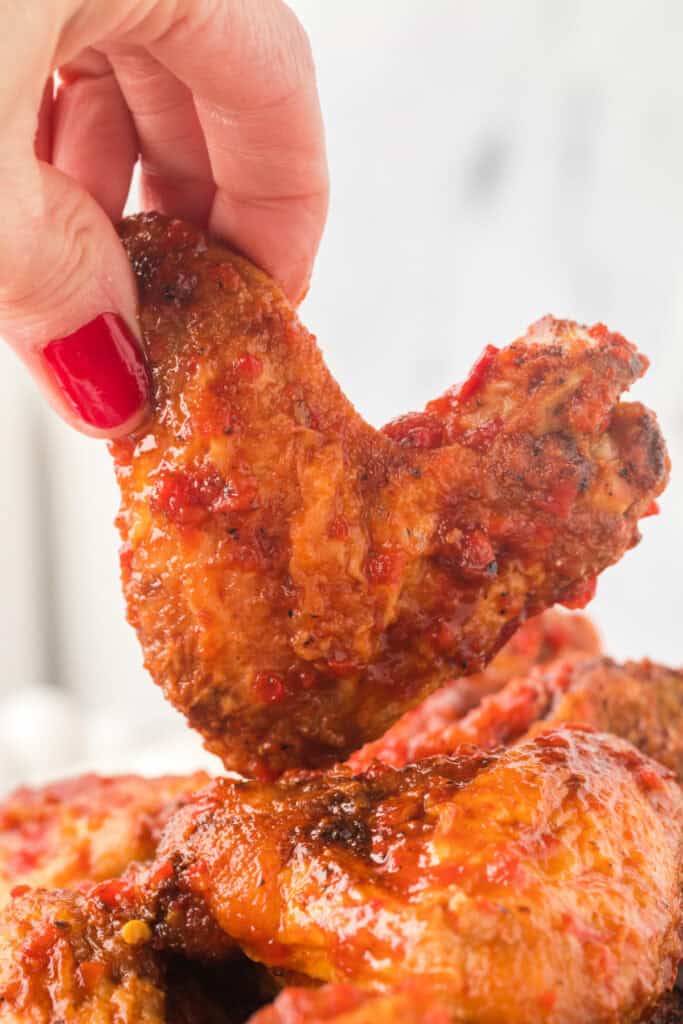 Close-up of a hand holding a saucy chipotle honey chicken wing with red nail polish.