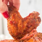 Hand holding a crispy chipotle honey wing close up, highlighting the saucy coating and charred edges.