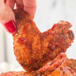 Hand holding a crispy chipotle honey wing close up, highlighting the saucy coating and charred edges.