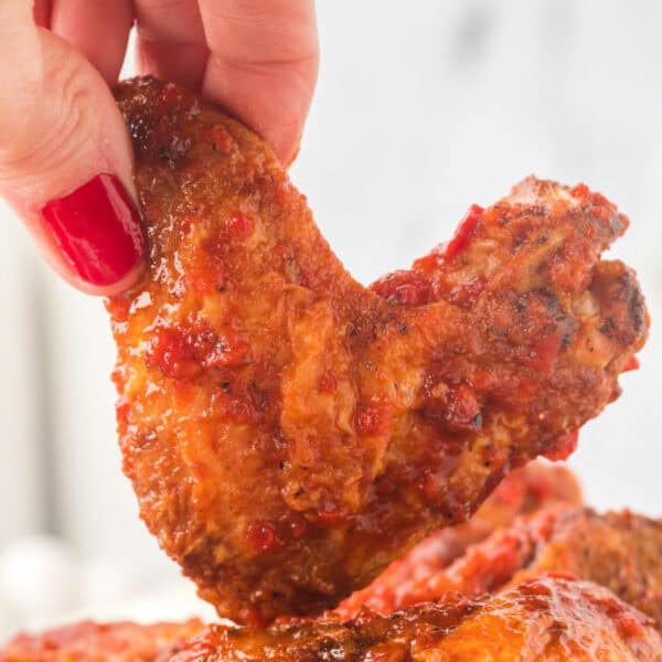 Hand holding a crispy chipotle honey wing close up, highlighting the saucy coating and charred edges.