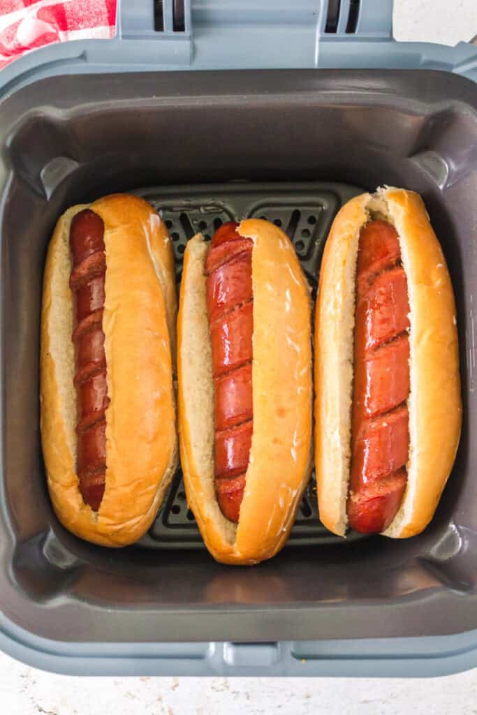 Three hot dogs placed in buns inside the air fryer ready to be toasted