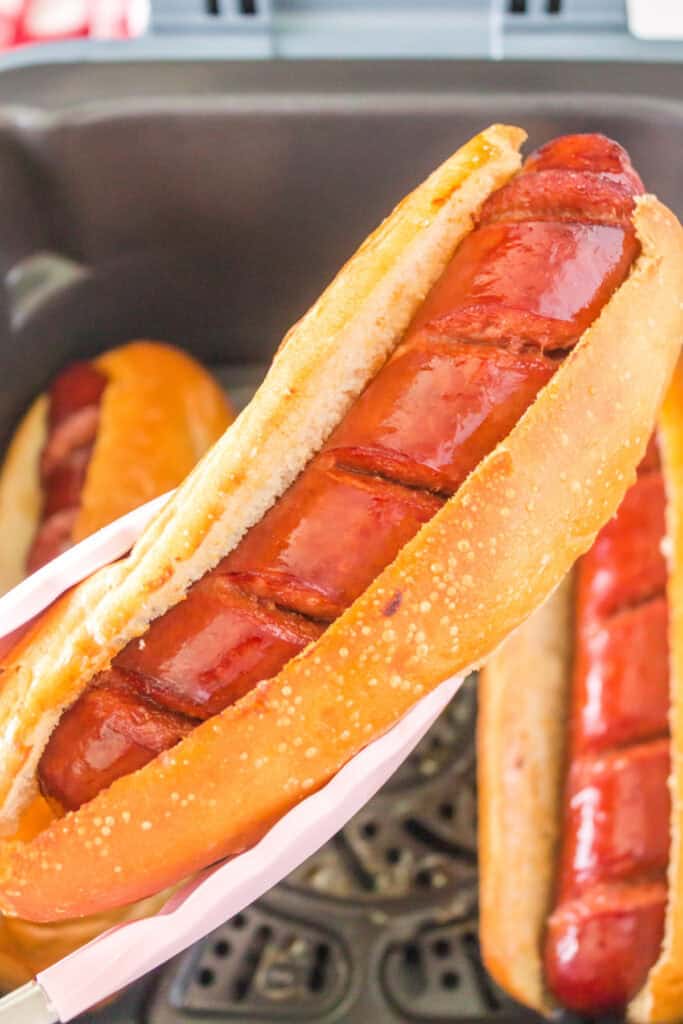 Tongs holding a crispy hot dog in a toasted hoagie bun