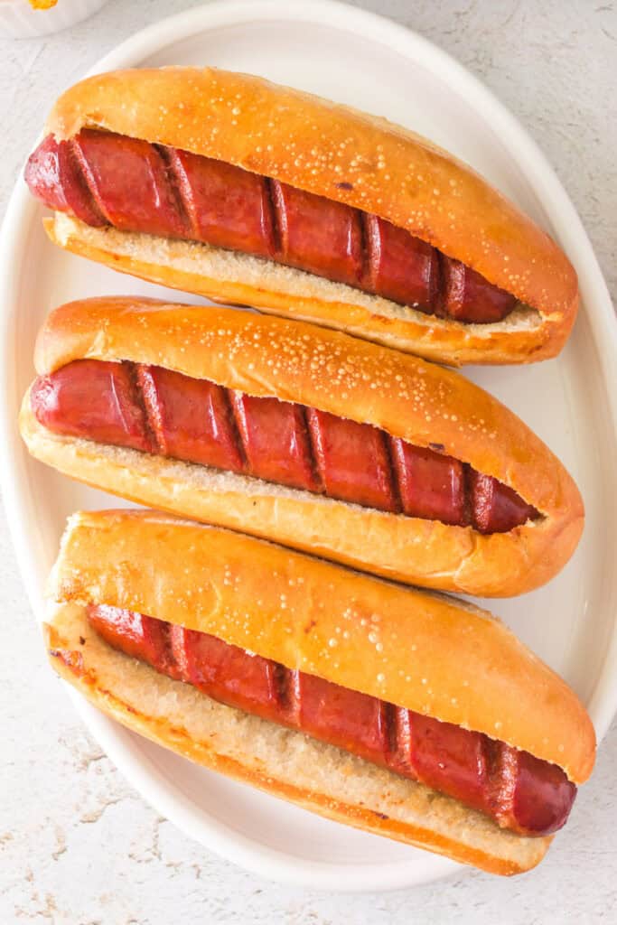 Three fully cooked hot dogs in toasted hoagie buns on a white platter