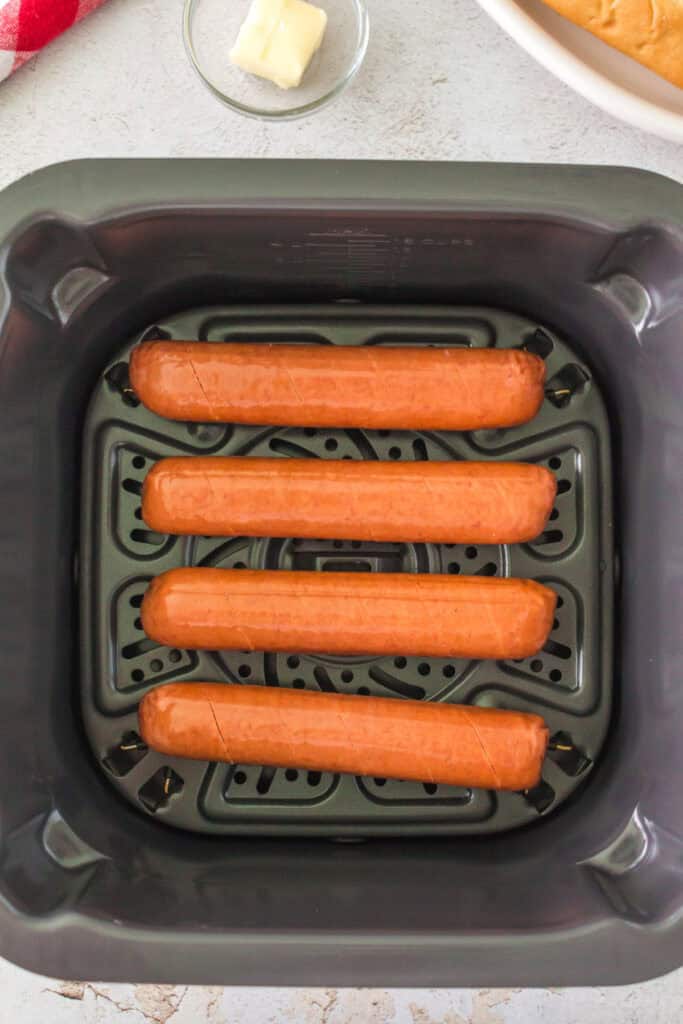 Four raw scored hot dog sausages placed in an air fryer basket
