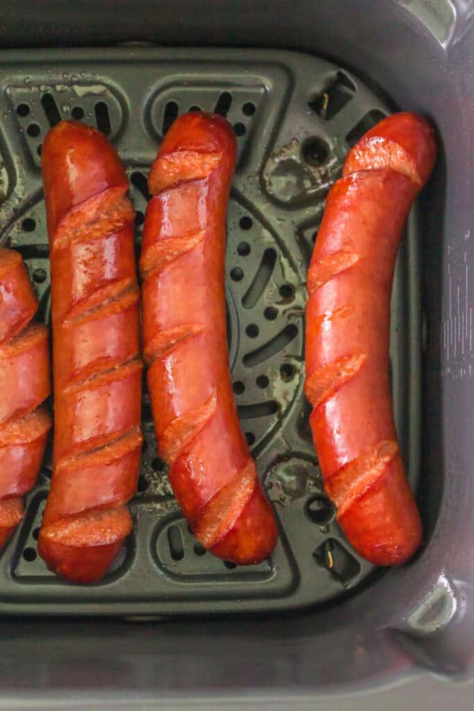 Hot dogs halfway cooked, skin starting to crisp inside air fryer