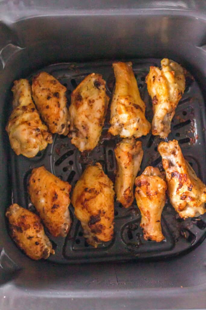 Golden brown lemon pepper chicken wings cooking in an air fryer basket.