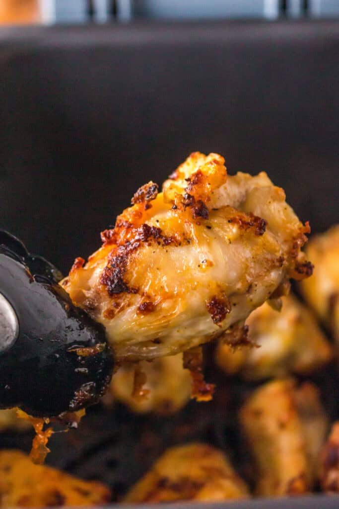Close-up of crispy air fryer lemon pepper chicken wing held with tongs over the basket.
