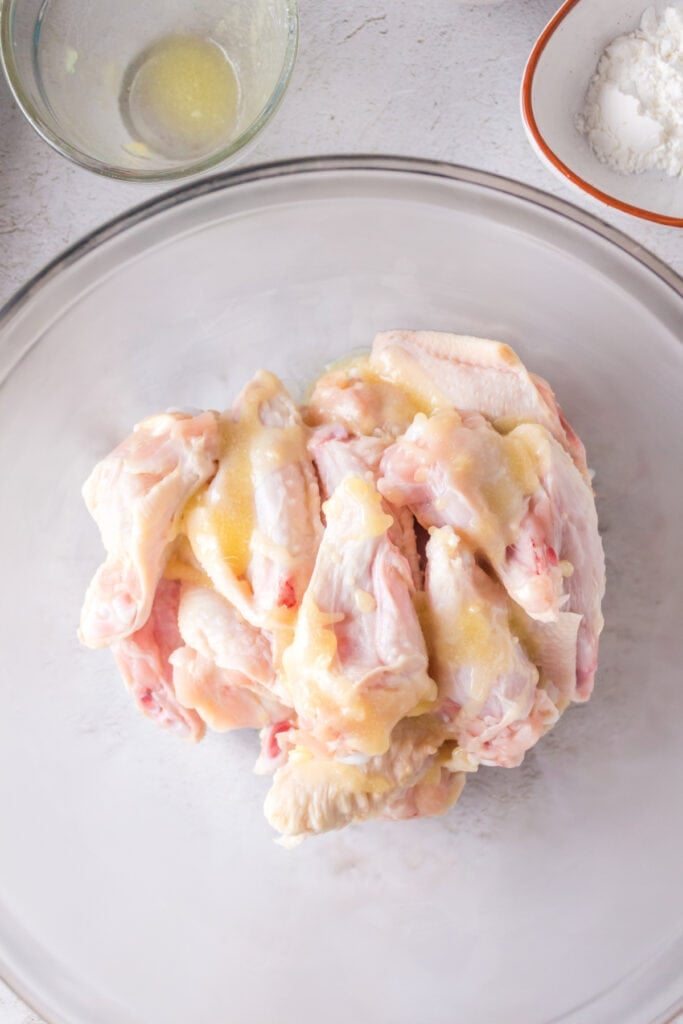 Raw chicken wings drizzled with melted butter in a clear mixing bowl.