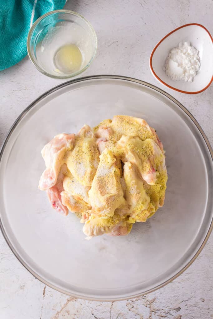 Chicken wings in a bowl sprinkled with lemon pepper seasoning mix.