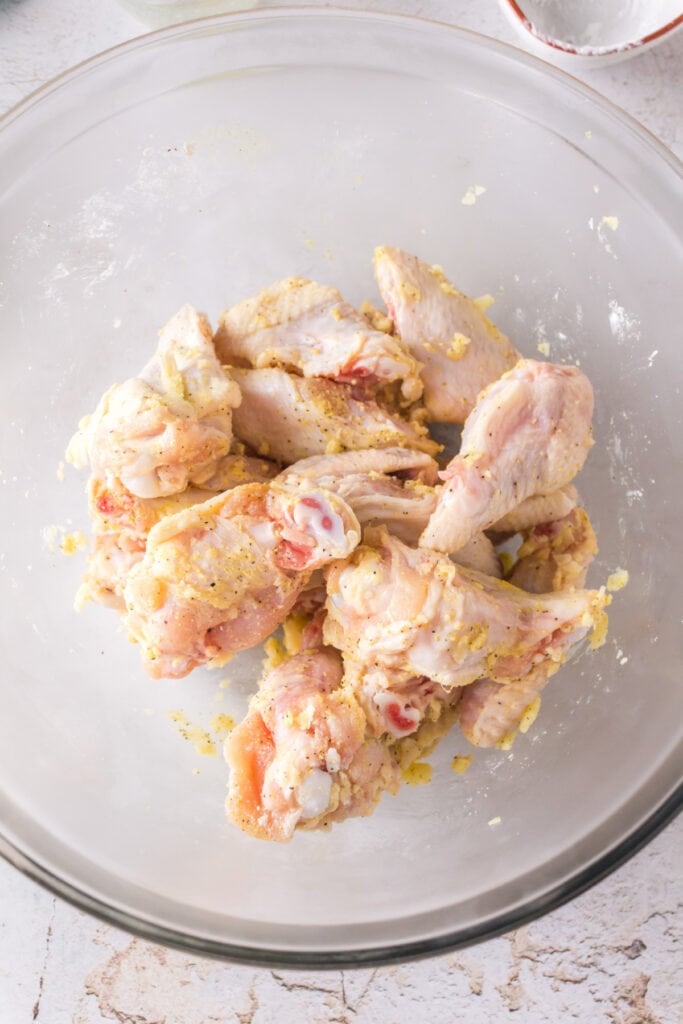Seasoned and coated raw chicken wings tossed together in a mixing bowl.