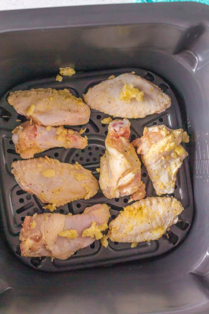 Uncooked seasoned chicken wings arranged in a single layer in the air fryer basket.