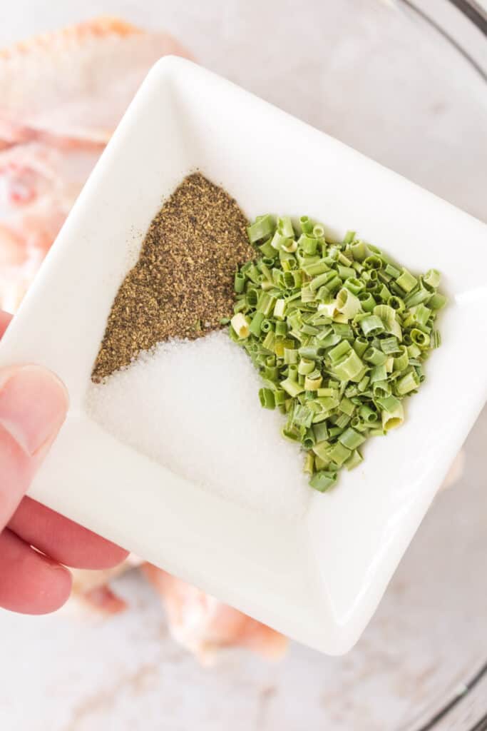 Small dish holding dry chives, ground black pepper, and salt for seasoning chicken wings