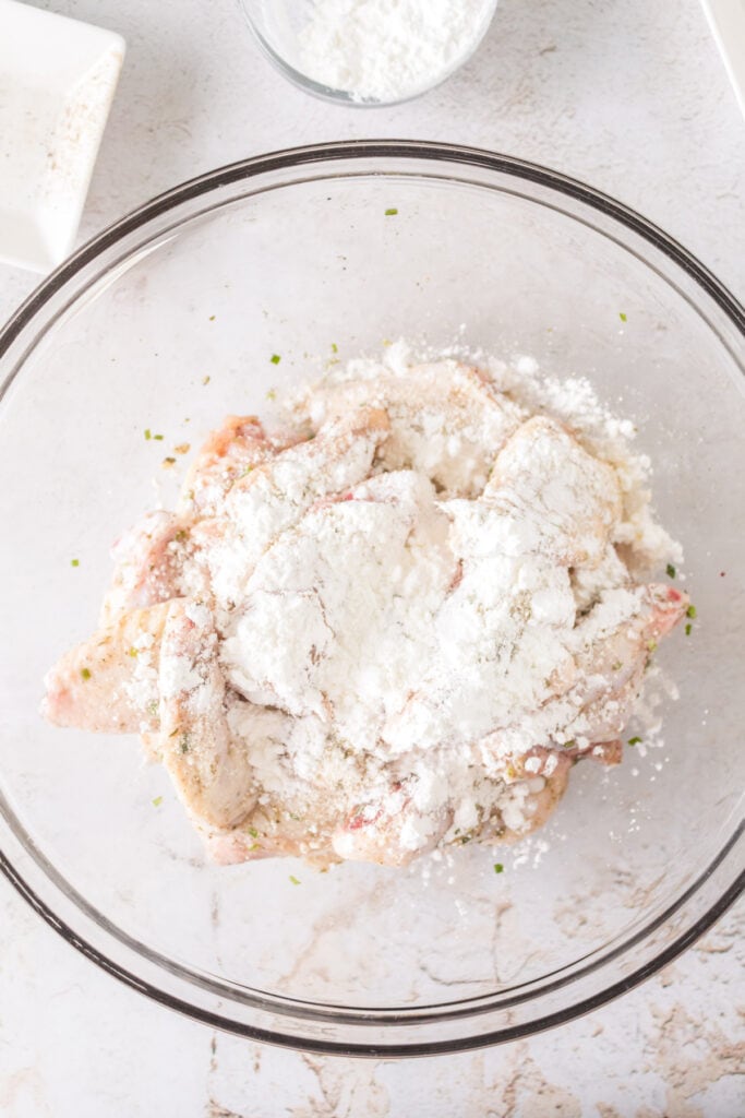 Chicken wings sprinkled with cornstarch in a glass bowl before tossing