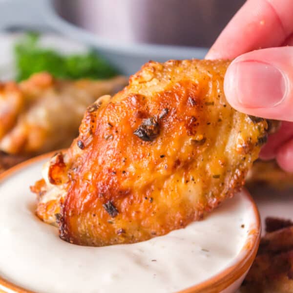 Close-up square photo of crispy air fryer ranch wings dipped in creamy ranch sauce