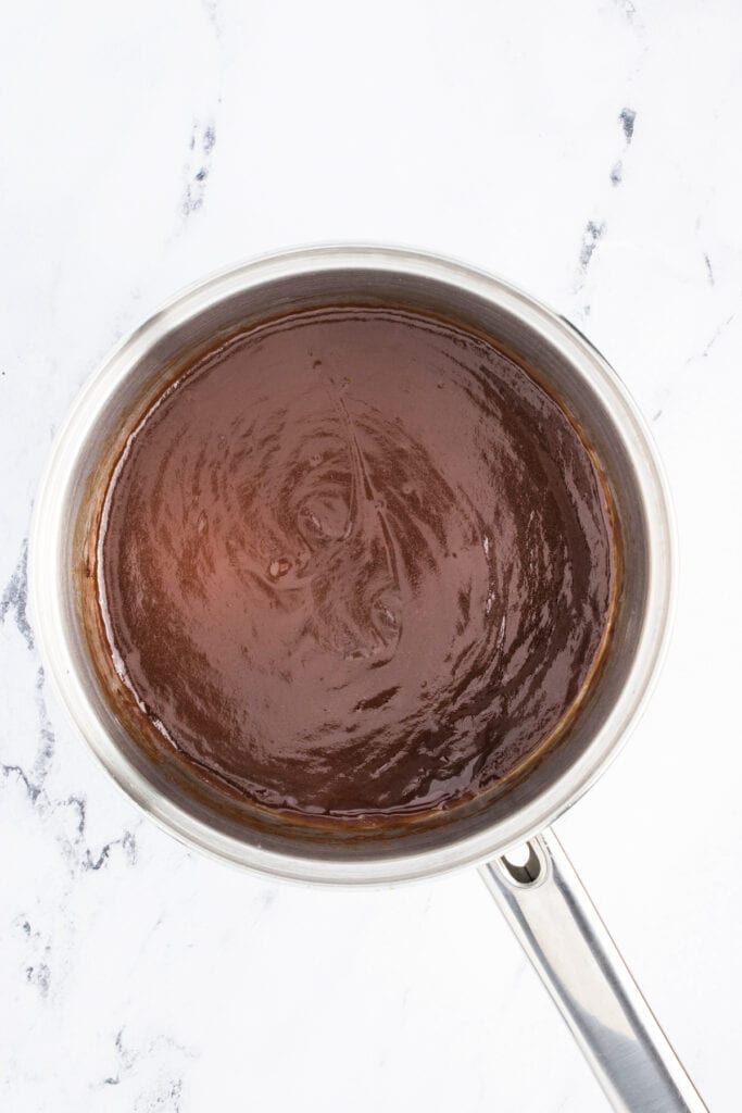 Saucepan filled with thick, glossy homemade sesame chicken sauce simmering on a stovetop.