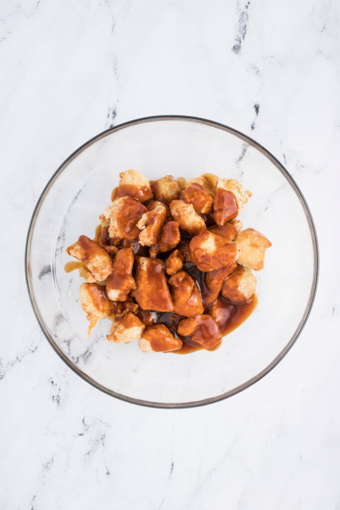 Crispy chicken pieces in a glass bowl topped with freshly made sesame sauce before tossing.