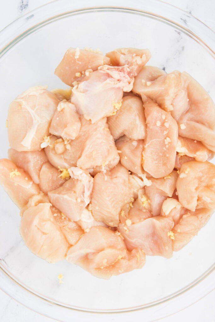 Glass bowl filled with chicken chunks mixed with garlic and ginger, ready to be marinated.