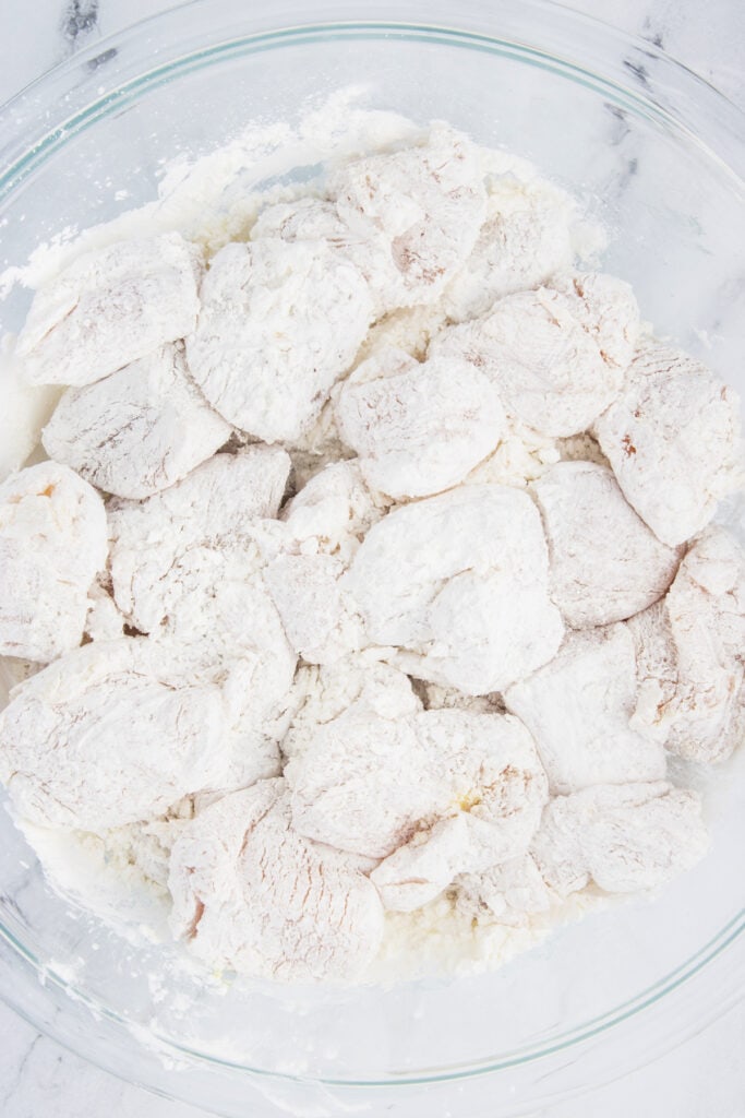 Raw chicken pieces coated in cornstarch in a glass bowl, fully covered and ready for air frying.