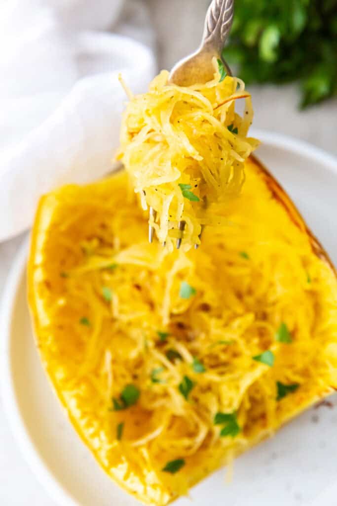 Cooked spaghetti squash strands lifted with a fork, garnished with parsley, inside the squash shell.