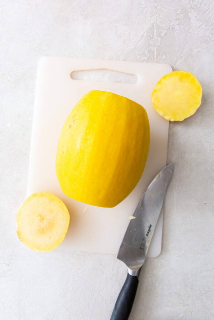 Spaghetti squash with the ends cut off sitting on a cutting board beside a knife.