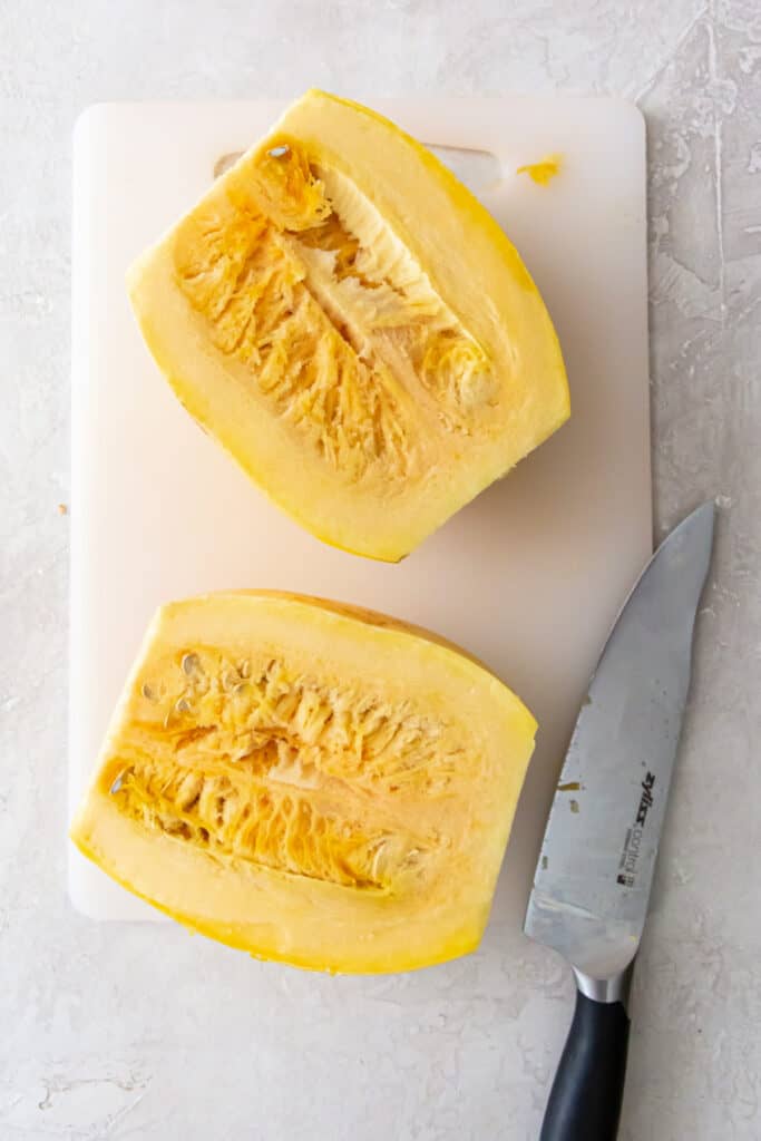 Spaghetti squash sliced in half lengthwise on a cutting board, showing the inside with seeds.