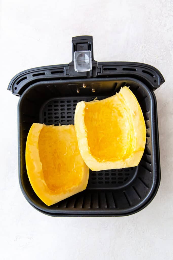 Two cleaned spaghetti squash halves placed cut side up in an air fryer basket.