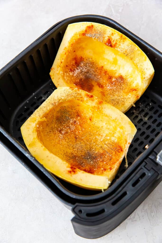 Spaghetti squash halves in an air fryer basket seasoned with paprika, salt, and pepper.