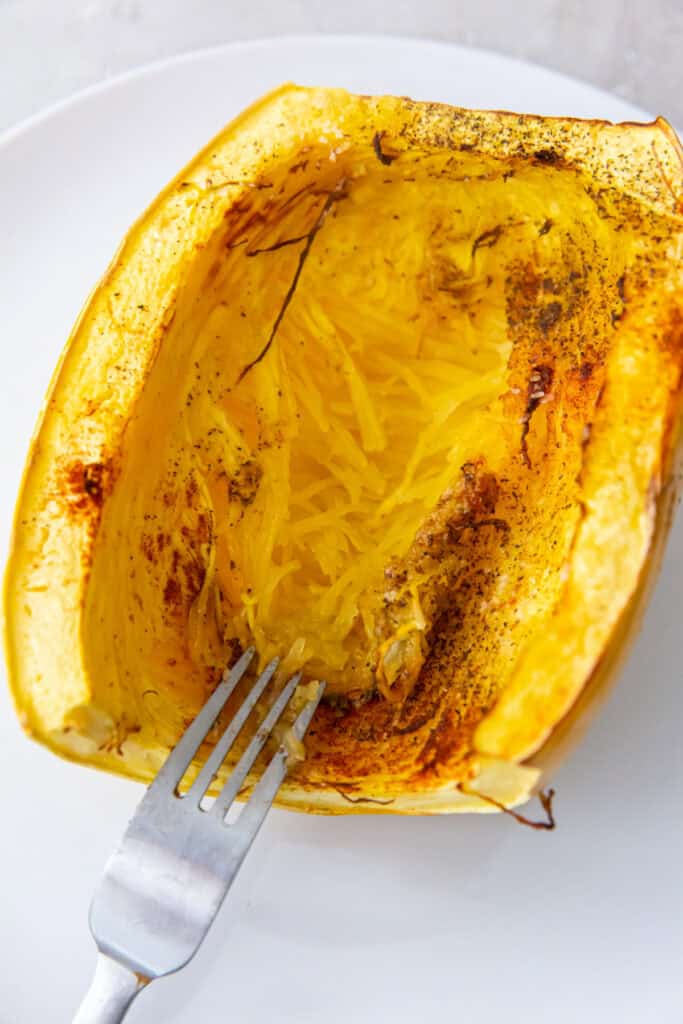 Fork scraping strands from the roasted spaghetti squash inside its shell.