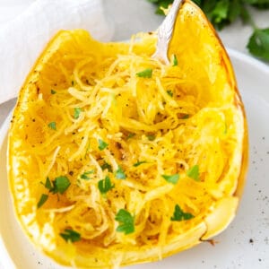 Close-up of roasted spaghetti squash half with fork and parsley garnish, square crop for social sharing.