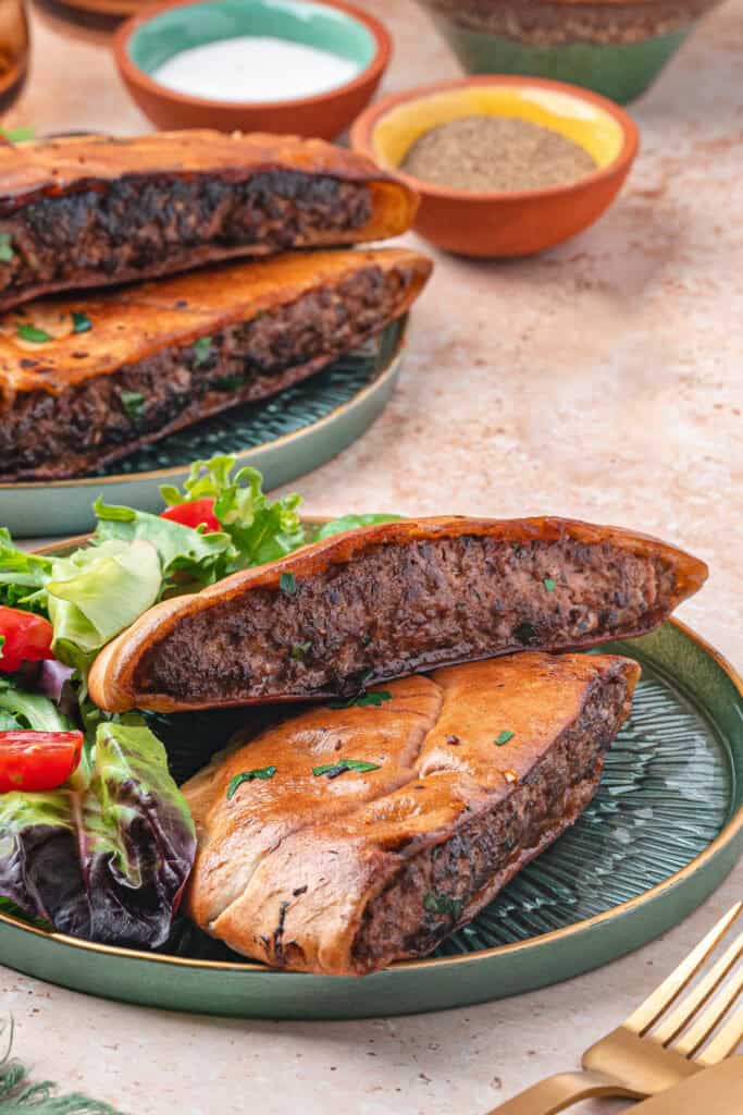 Two arayes halves on a green plate with fresh salad on the side, showing the cooked meat filling inside the crispy pita bread.