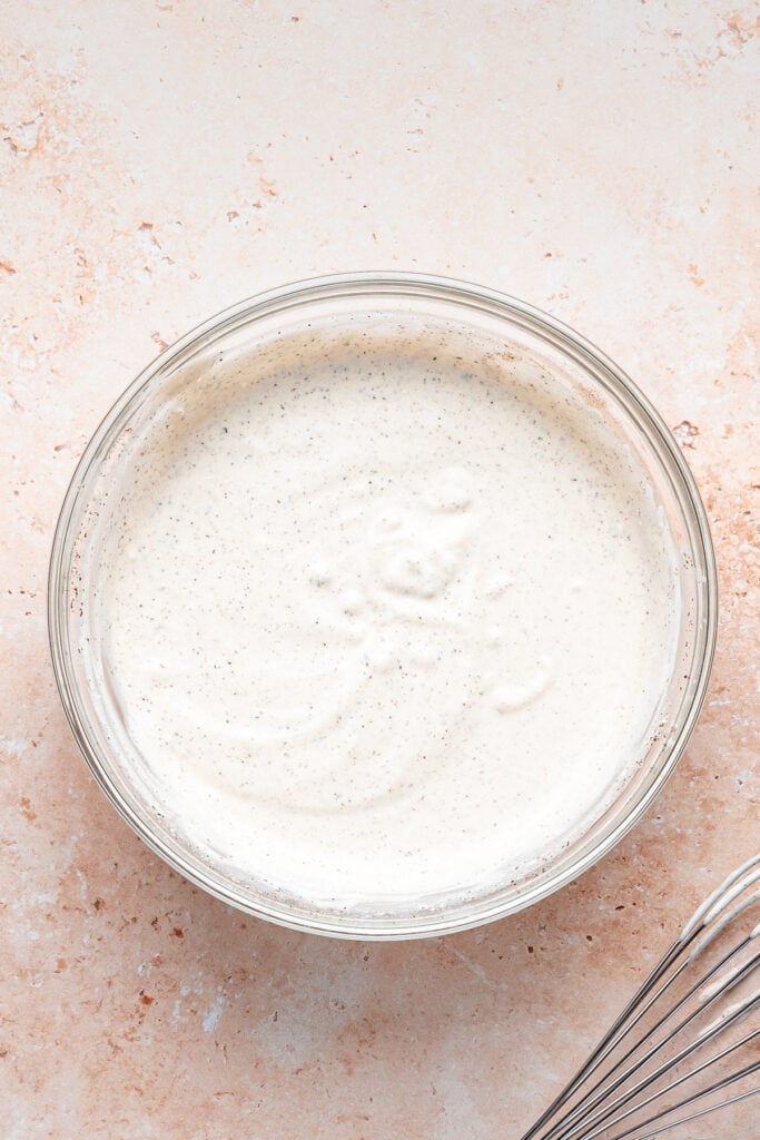 Smooth and creamy shwarma white sauce whisked together in a glass bowl with a whisk nearby.