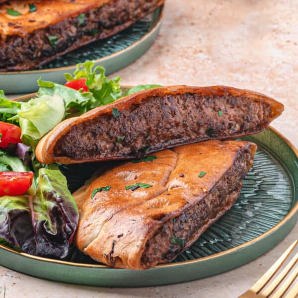 Square crop of arayes served on a green plate with salad, showing the crisp pita and spiced meat filling inside.