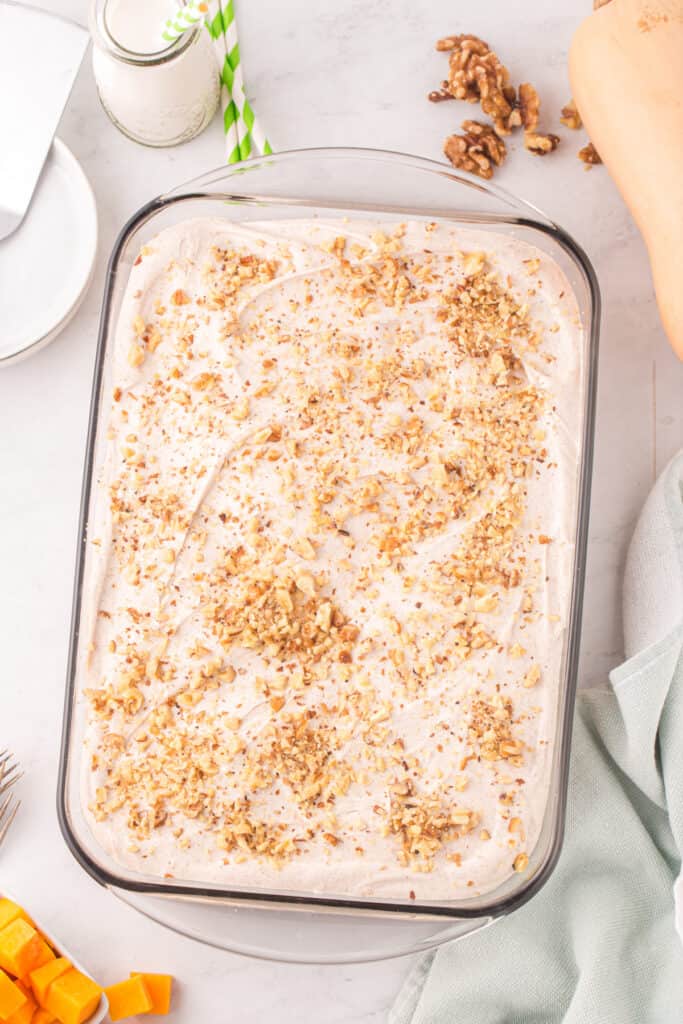 Finished butternut squash cake frosted with cream cheese frosting and sprinkled with chopped walnuts in a glass baking dish.