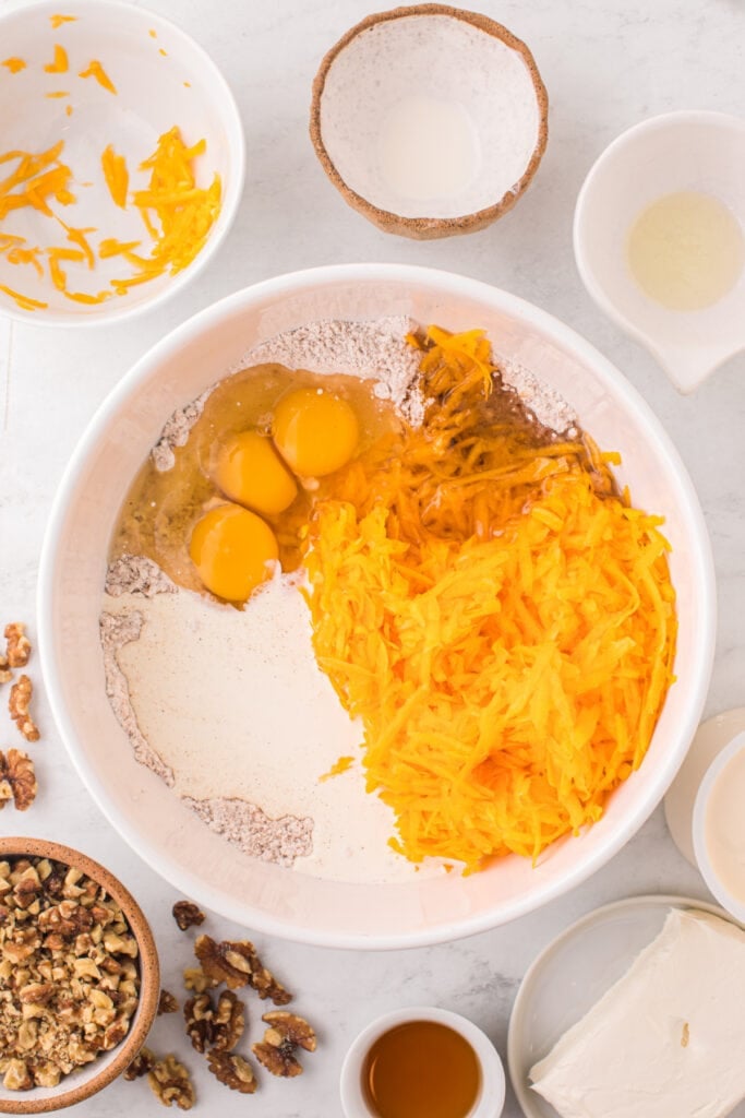 Large mixing bowl with grated butternut squash, eggs, oil, cream, and dry cake mix ready to be mixed together.