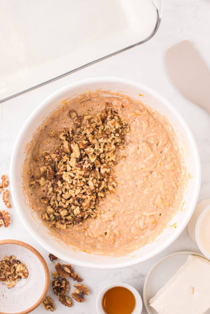 Bowl of butternut squash cake batter with chopped walnuts added on top, ready to be stirred in.