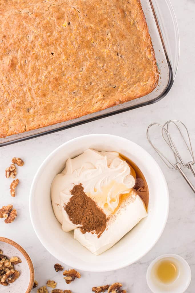 Baked butternut squash cake in a glass dish next to a bowl of cream cheese frosting ingredients.