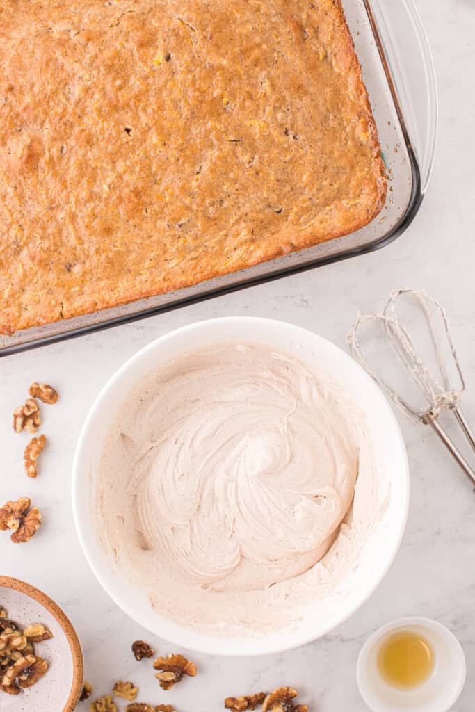 Bowl of cream cheese frosting beaten until smooth and fluffy next to the cooled butternut squash cake.