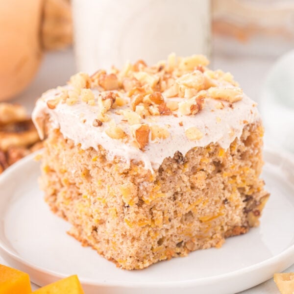Square-cropped image of a frosted slice of butternut squash cake with walnuts on a white plate.