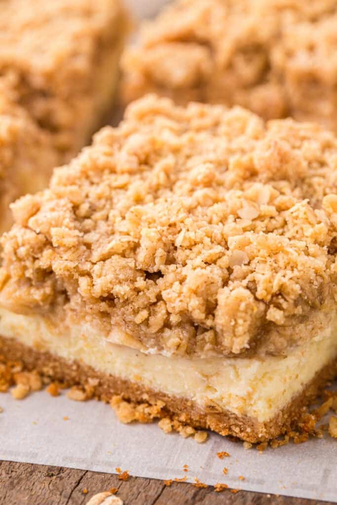 Side view of cheesecake bars with layers of graham cracker crust, cheesecake, apples, and crumble.