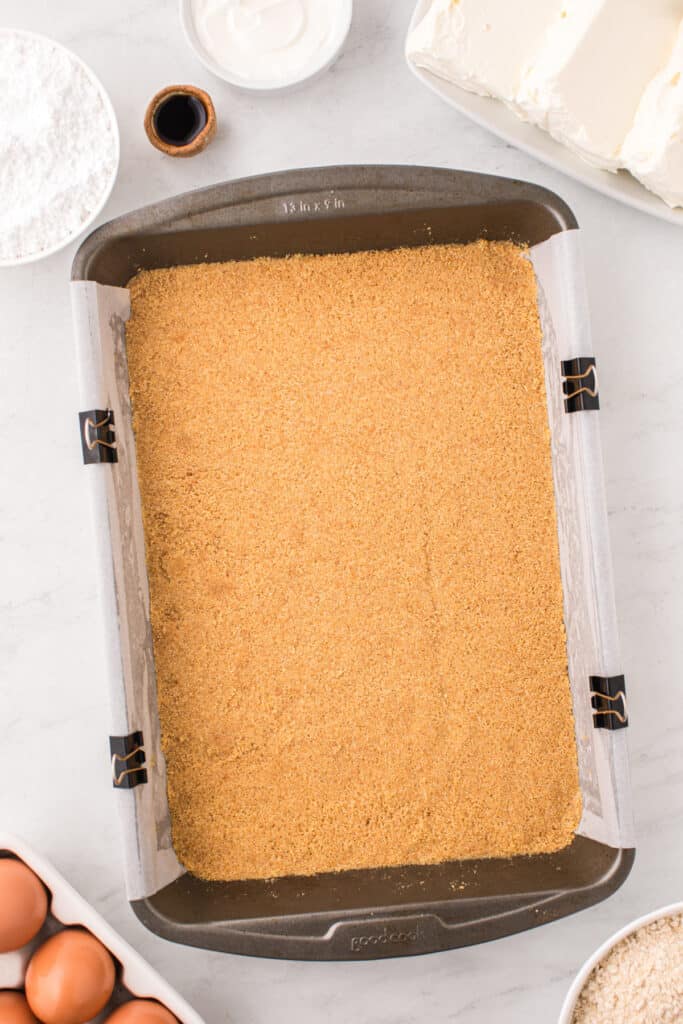Pressed graham cracker crust in a parchment-lined 9x13-inch baking pan.