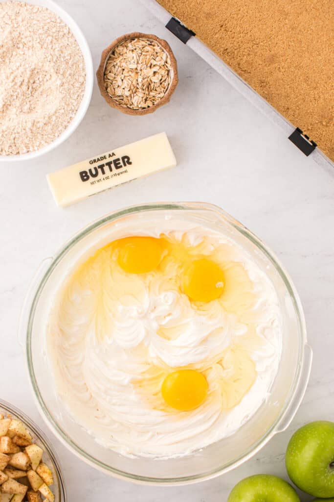 Cream cheese filling in a bowl with cracked eggs added before mixing.