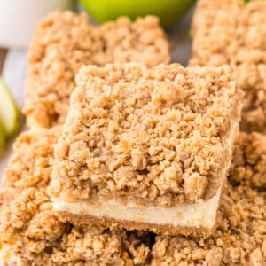 Square cut caramel apple cheesecake bar with crumb topping, styled on parchment paper.
