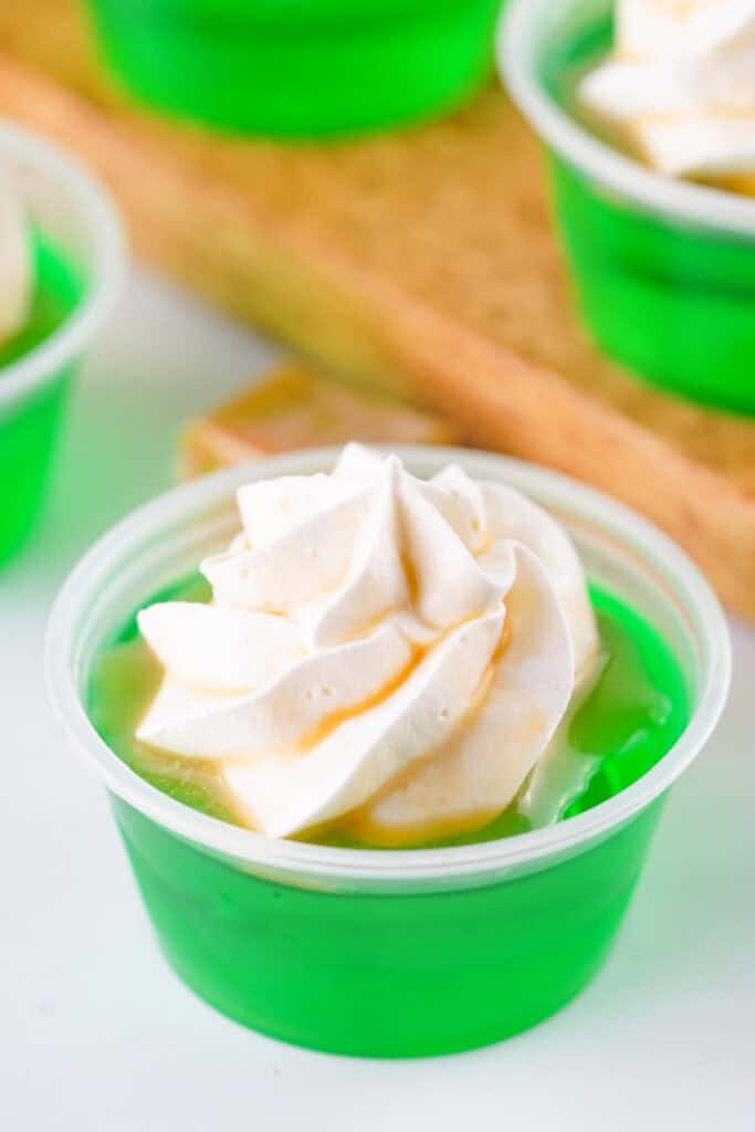 Close-up of a finished caramel apple jello shot topped with whipped cream and caramel drizzle.