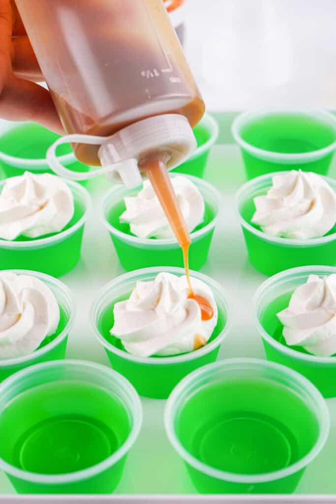 Caramel sauce being drizzled over whipped topping on finished caramel apple jello shots.
