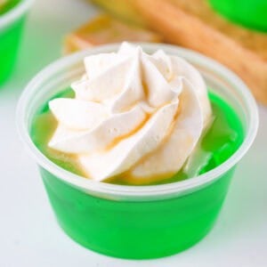 Square image of a caramel apple jello shot topped with whipped cream and caramel drizzle, perfect for social media sharing.