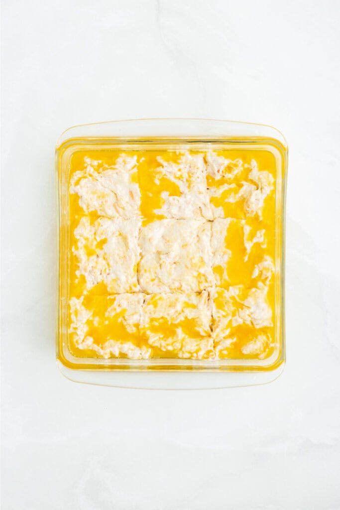 Biscuit dough scored into 9 squares in the butter-filled baking dish, ready to bake.